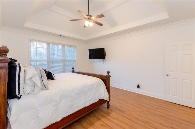 bedroom with light wood-style flooring, crown molding, a tray ceiling, and baseboards