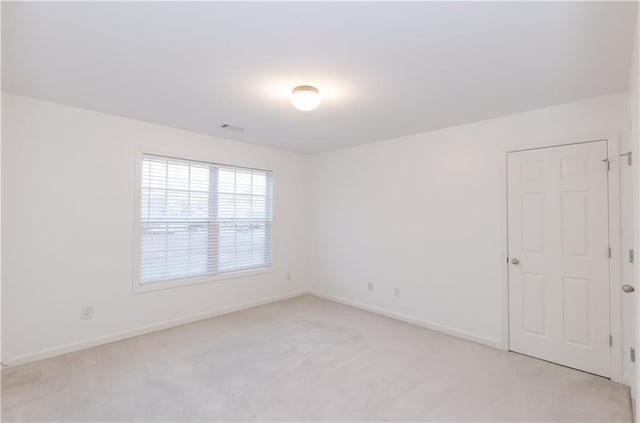 empty room with baseboards, visible vents, and light colored carpet