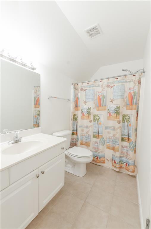 full bath with toilet, vanity, visible vents, vaulted ceiling, and tile patterned floors