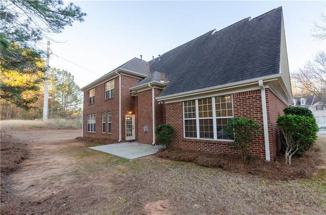 rear view of property featuring a shingled roof, a patio, and brick siding