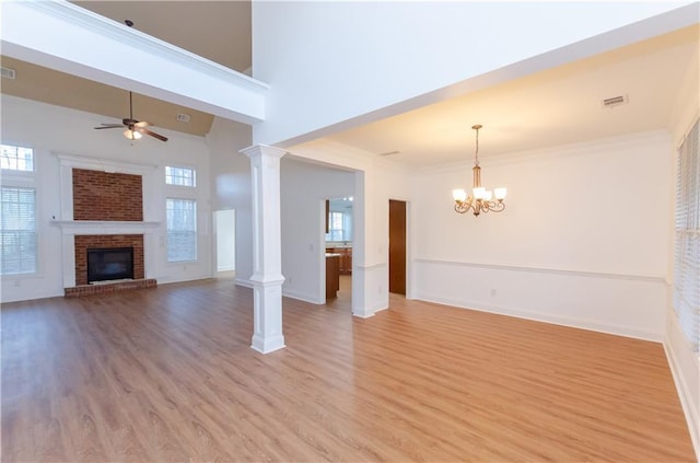 unfurnished living room featuring a fireplace, plenty of natural light, ornate columns, and ceiling fan with notable chandelier