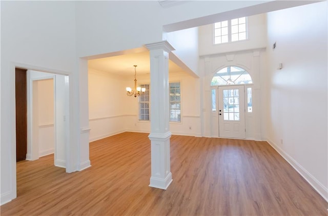 foyer with light wood-type flooring, decorative columns, a towering ceiling, and baseboards