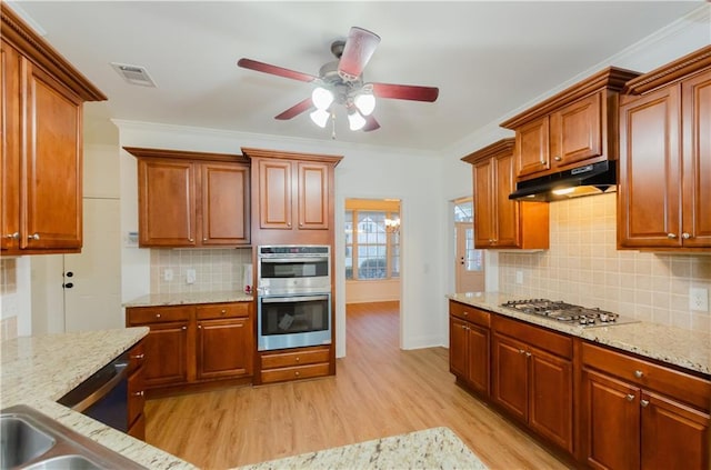 kitchen featuring crown molding, light wood finished floors, stainless steel appliances, light stone countertops, and under cabinet range hood