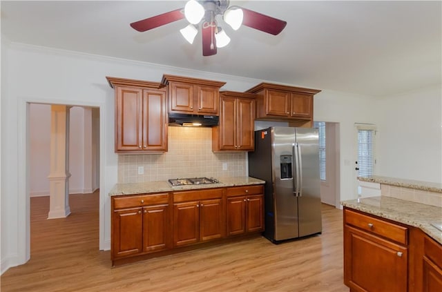 kitchen with light wood-style flooring, under cabinet range hood, ornamental molding, appliances with stainless steel finishes, and backsplash