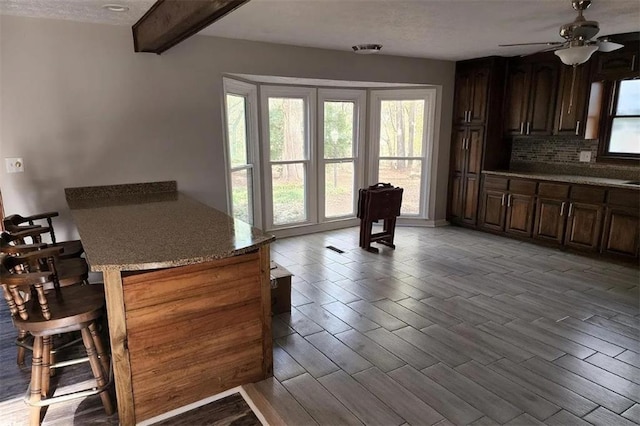 kitchen featuring light stone countertops, backsplash, ceiling fan, beam ceiling, and light hardwood / wood-style flooring