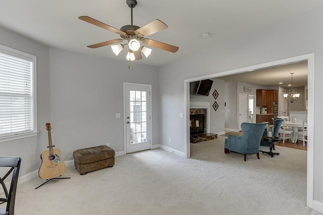 living area featuring a high end fireplace, ceiling fan with notable chandelier, and light colored carpet