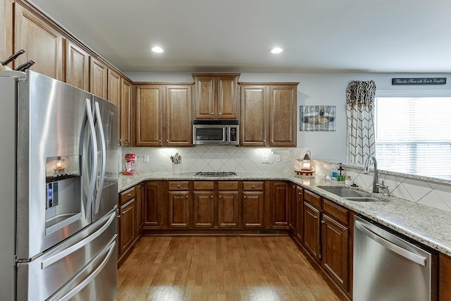 kitchen with tasteful backsplash, light wood-type flooring, appliances with stainless steel finishes, light stone countertops, and sink