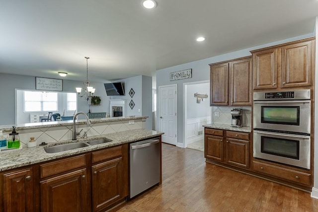 kitchen with wood-type flooring, appliances with stainless steel finishes, decorative light fixtures, light stone countertops, and sink