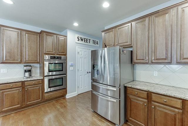 kitchen with appliances with stainless steel finishes, decorative backsplash, light stone counters, and light hardwood / wood-style floors