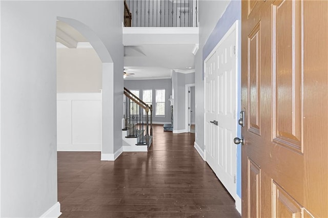 foyer entrance with a wainscoted wall, ceiling fan, stairs, dark wood-type flooring, and a decorative wall