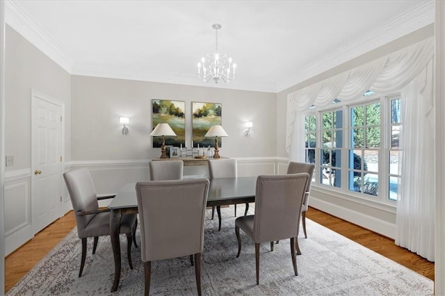 dining room with wood finished floors, ornamental molding, a notable chandelier, and wainscoting