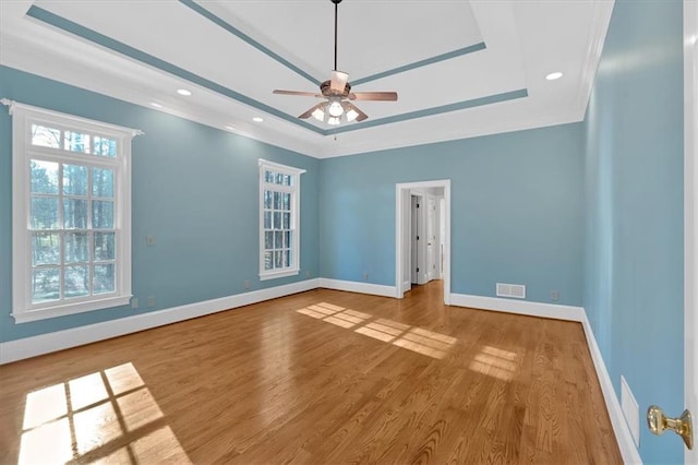 spare room with baseboards, visible vents, wood finished floors, ceiling fan, and a raised ceiling