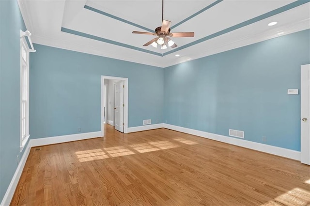 spare room featuring a raised ceiling, baseboards, wood finished floors, ceiling fan, and ornamental molding