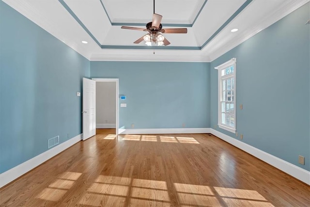 empty room with a tray ceiling, visible vents, wood finished floors, ceiling fan, and crown molding