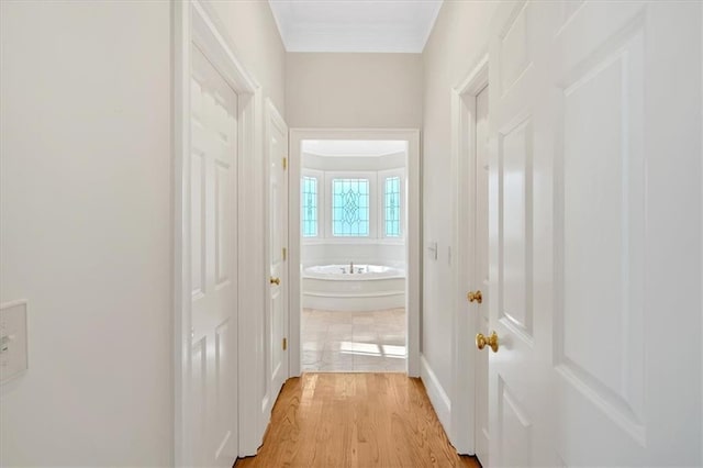 hallway with baseboards, ornamental molding, and light wood-type flooring