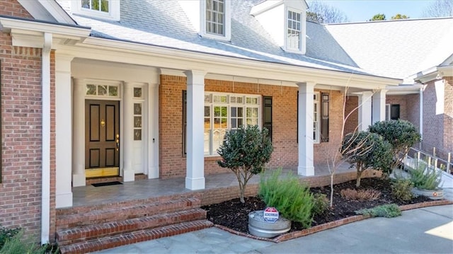 doorway to property featuring covered porch and brick siding