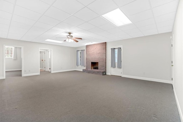 unfurnished living room featuring baseboards, a paneled ceiling, a brick fireplace, and dark colored carpet
