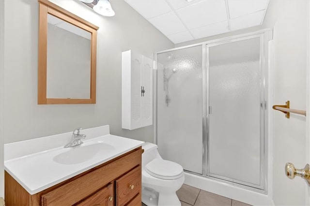 bathroom with a shower stall, tile patterned floors, vanity, a drop ceiling, and toilet