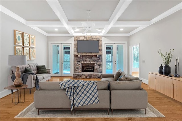 living area featuring french doors, light wood-type flooring, baseboards, beamed ceiling, and a stone fireplace