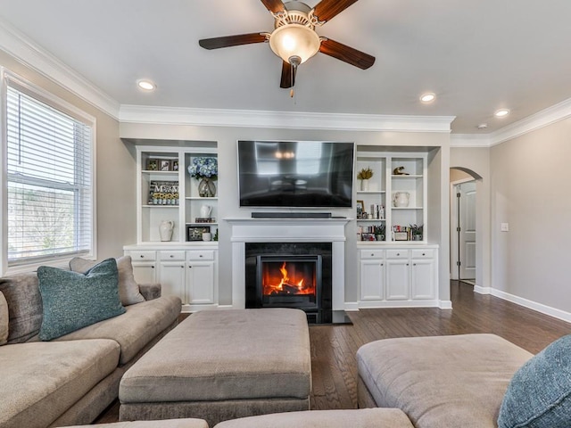 living area with arched walkways, a warm lit fireplace, crown molding, and dark wood-type flooring