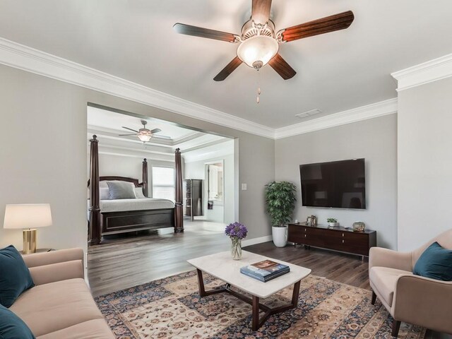 living area featuring wood finished floors, baseboards, visible vents, ceiling fan, and ornamental molding