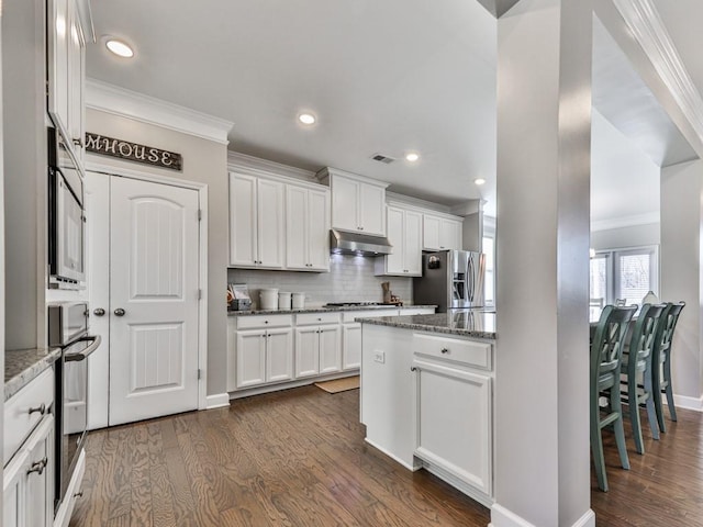 kitchen featuring visible vents, under cabinet range hood, dark wood finished floors, ornamental molding, and appliances with stainless steel finishes