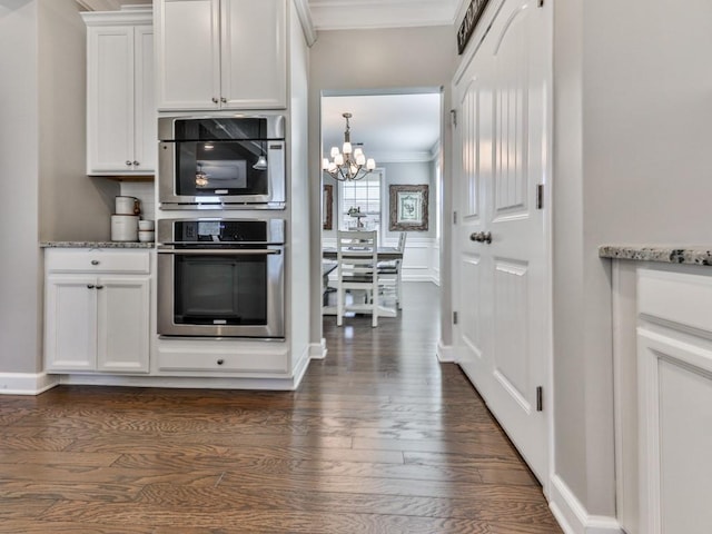 kitchen with light stone counters, dark wood finished floors, ornamental molding, white cabinets, and a decorative wall