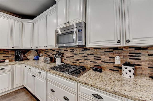 kitchen with appliances with stainless steel finishes, light hardwood / wood-style flooring, light stone counters, white cabinetry, and decorative backsplash