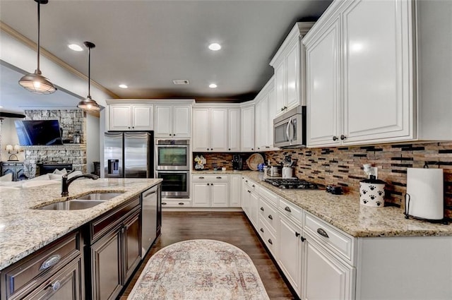 kitchen featuring stainless steel appliances, light stone counters, white cabinets, pendant lighting, and sink