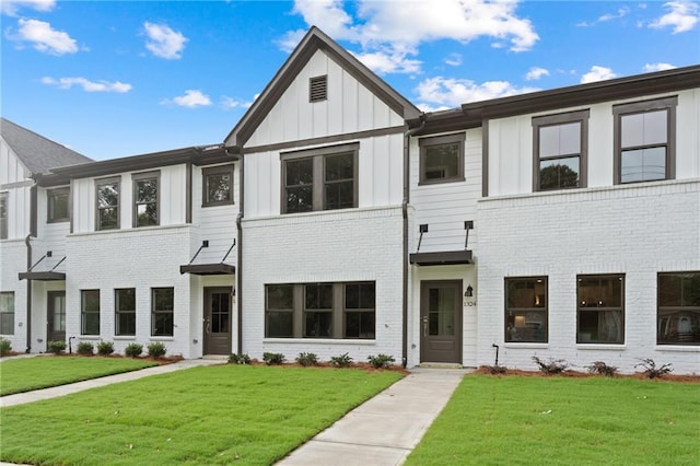 townhome / multi-family property featuring a front yard, board and batten siding, and brick siding