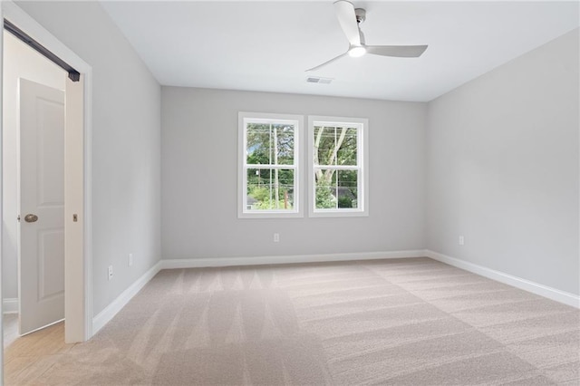 empty room featuring ceiling fan, visible vents, baseboards, and light colored carpet