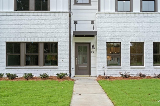 entrance to property with brick siding, board and batten siding, and a yard