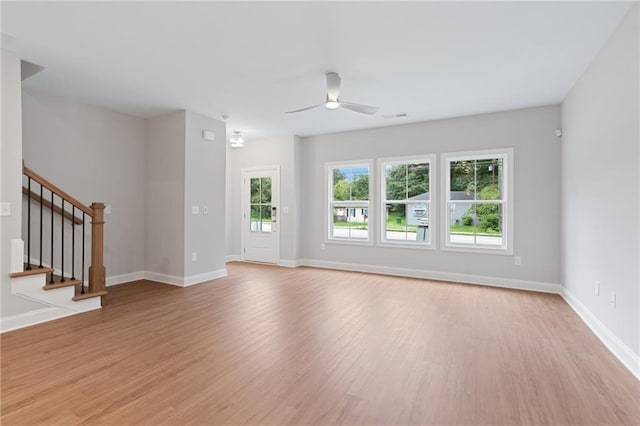 unfurnished living room featuring stairs, ceiling fan, light wood-type flooring, and baseboards