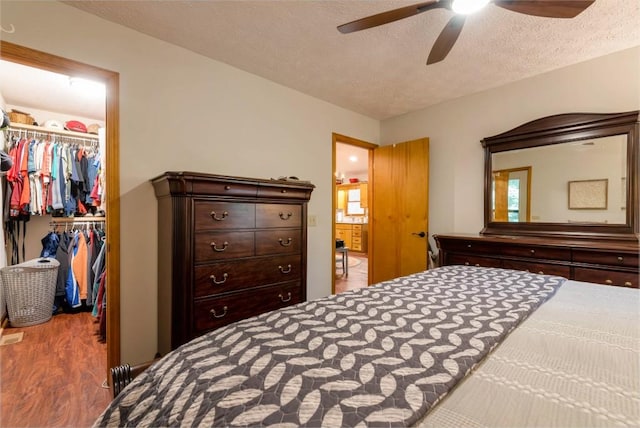 bedroom with ceiling fan, wood-type flooring, a textured ceiling, a walk in closet, and a closet