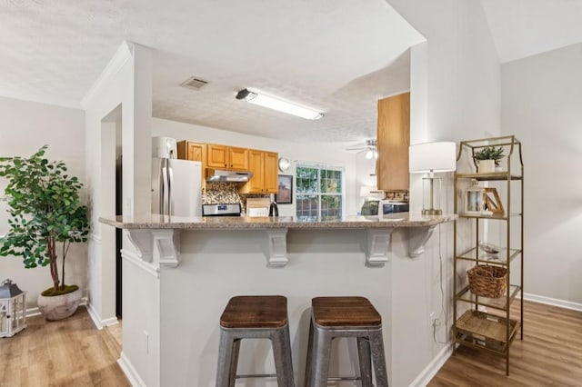 2277 Lazy Days Rd, Dacula, GA 30019 - kitchen with freestanding refrigerator, under cabinet range hood, range, light wood finished floors, and a breakfast bar area