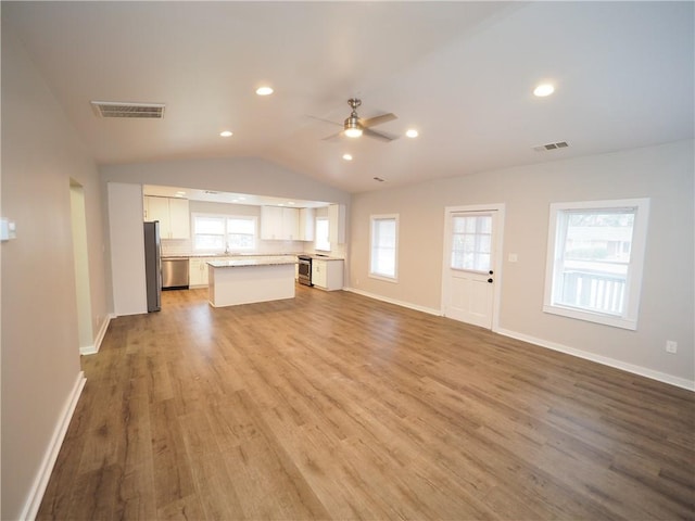 unfurnished living room featuring vaulted ceiling, a wealth of natural light, wood finished floors, and visible vents