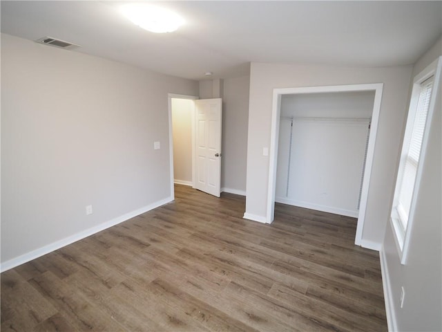 unfurnished bedroom with a closet, visible vents, baseboards, and wood finished floors