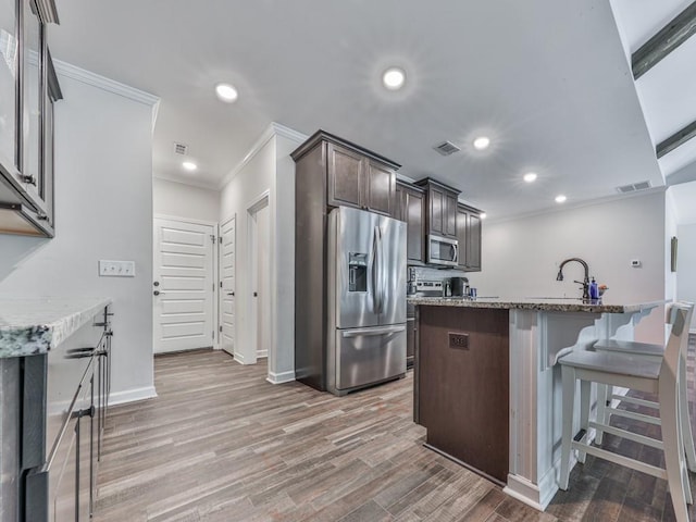 kitchen with appliances with stainless steel finishes, crown molding, dark brown cabinets, light stone countertops, and baseboards