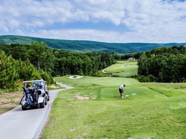 view of community featuring golf course view, a view of trees, driveway, and a yard