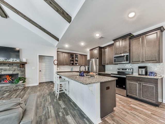 kitchen with appliances with stainless steel finishes, open floor plan, a kitchen breakfast bar, recessed lighting, and light stone counters
