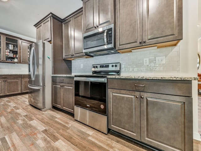 kitchen with appliances with stainless steel finishes, light wood-type flooring, decorative backsplash, light stone counters, and dark brown cabinets