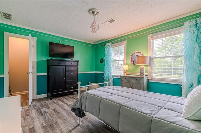 bedroom featuring light hardwood / wood-style floors, ornamental molding, and a textured ceiling