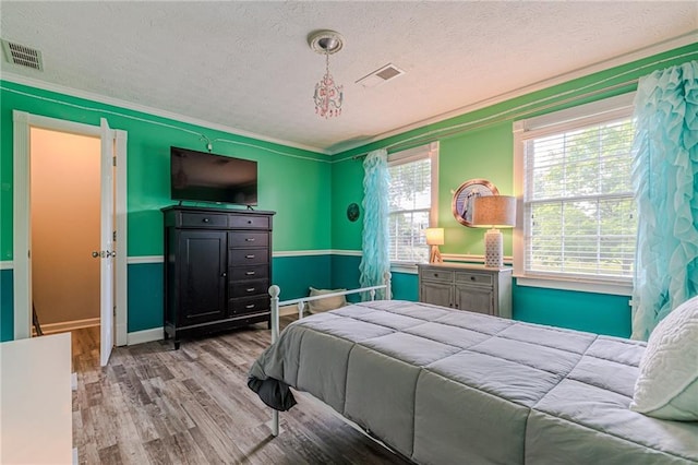 bedroom featuring light hardwood / wood-style floors, crown molding, and a textured ceiling