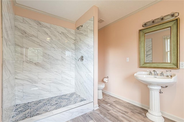 bathroom with crown molding, tiled shower, toilet, and hardwood / wood-style floors