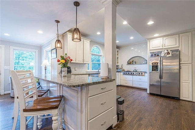 kitchen with appliances with stainless steel finishes, light stone counters, pendant lighting, a kitchen breakfast bar, and crown molding