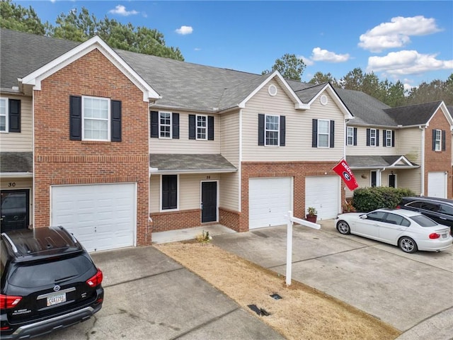 townhome / multi-family property featuring brick siding, driveway, an attached garage, and roof with shingles