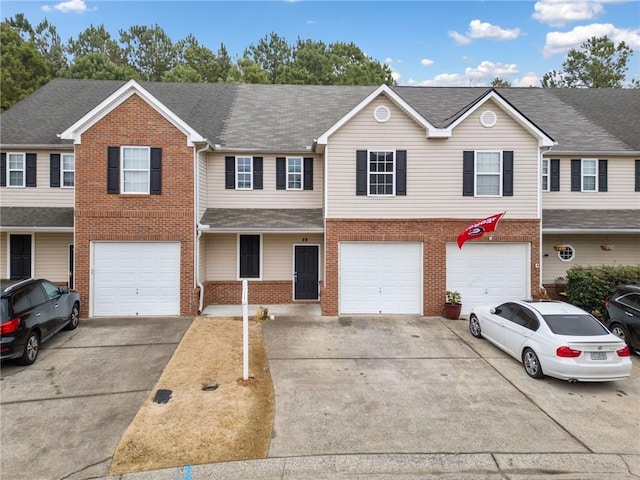 townhome / multi-family property with a shingled roof, brick siding, driveway, and an attached garage