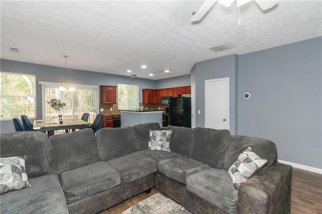 living room with a textured ceiling, dark hardwood / wood-style flooring, plenty of natural light, and ceiling fan with notable chandelier