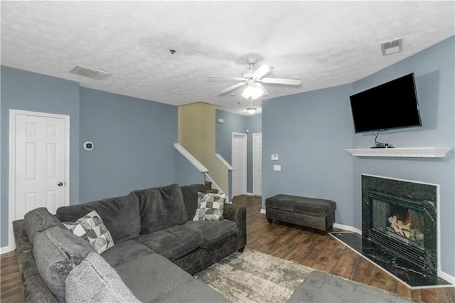 living room featuring ceiling fan, dark hardwood / wood-style flooring, a high end fireplace, and a textured ceiling