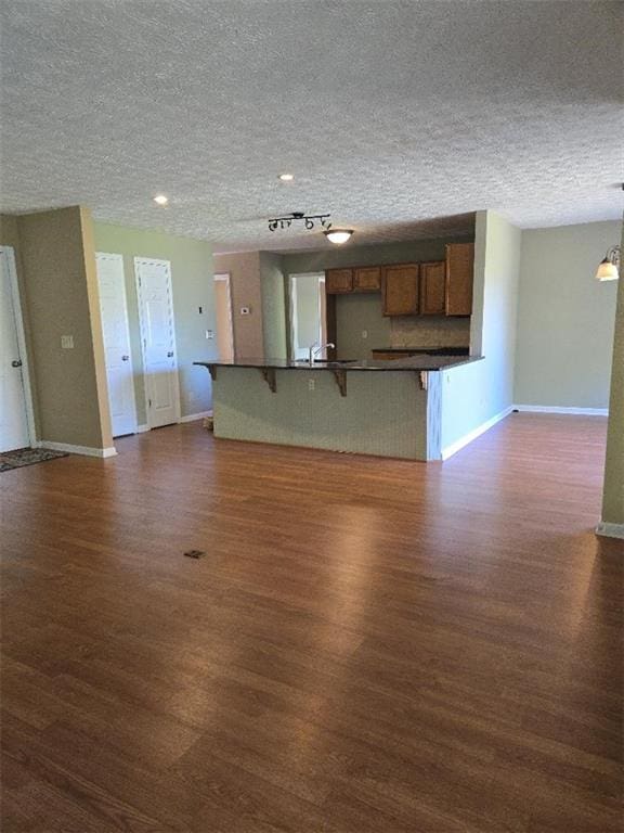 unfurnished living room with dark wood-style floors, a textured ceiling, and baseboards